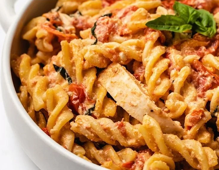 Baked feta chicken pasta served on a plate with fresh herbs and cherry tomatoes