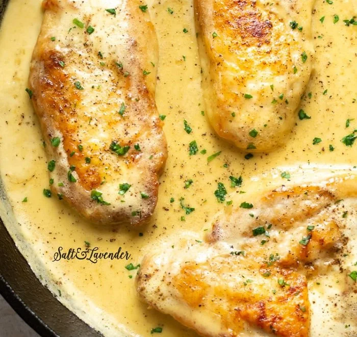 Creamy honey mustard chicken served on a plate with fresh herbs and vegetables.