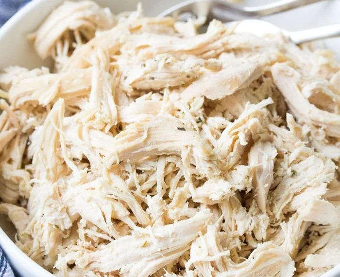 Crockpot shredded chicken in a bowl with herbs and spices