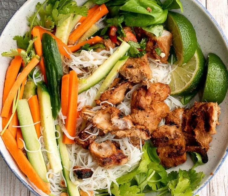 Vietnamese noodle bowl with lemongrass chicken, fresh herbs, and colorful vegetables