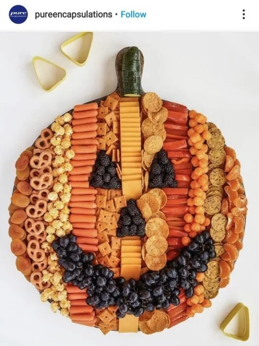 Colorful Halloween charcuterie board with pumpkins, snacks, cheeses, and spooky decorations.