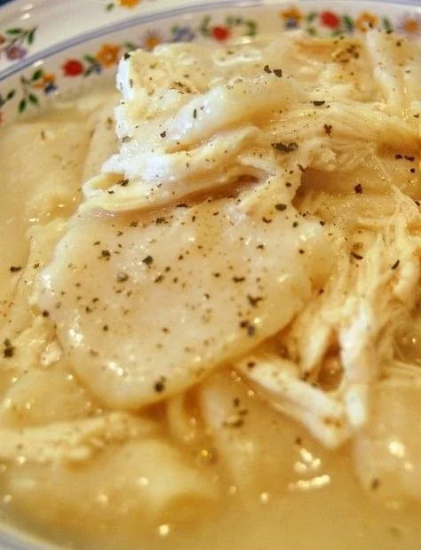 Bowl of homemade chicken and dumplings with fresh herbs on top